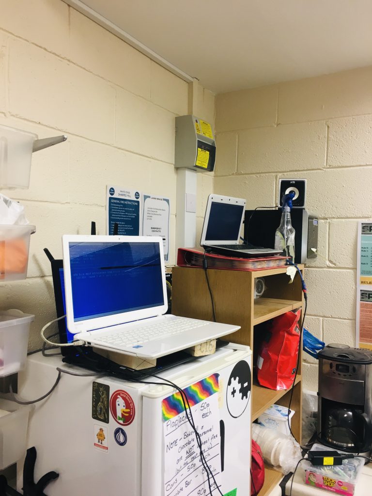 A black laptop on top of the fridge in the process of wiping with a white laptop on top of it separated by two wooden blocks also in the process of wiping. A small white laptop on top of a folder in the background in the process of wiping.