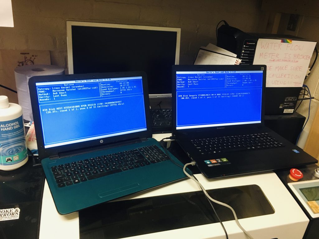 Two modern laptops on top of a laser cutter in the process of wiping their disks