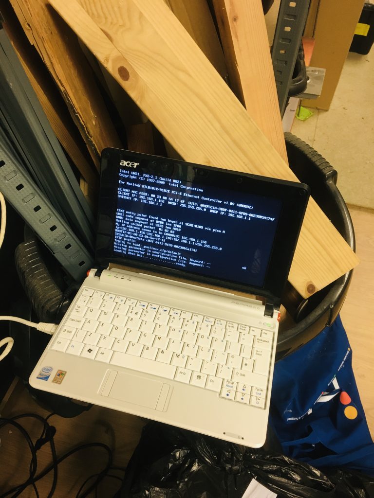 Small (10 inch or so) white laptop on top of a black round bin with wood cuts inside, with a white ethernet cable plugged in